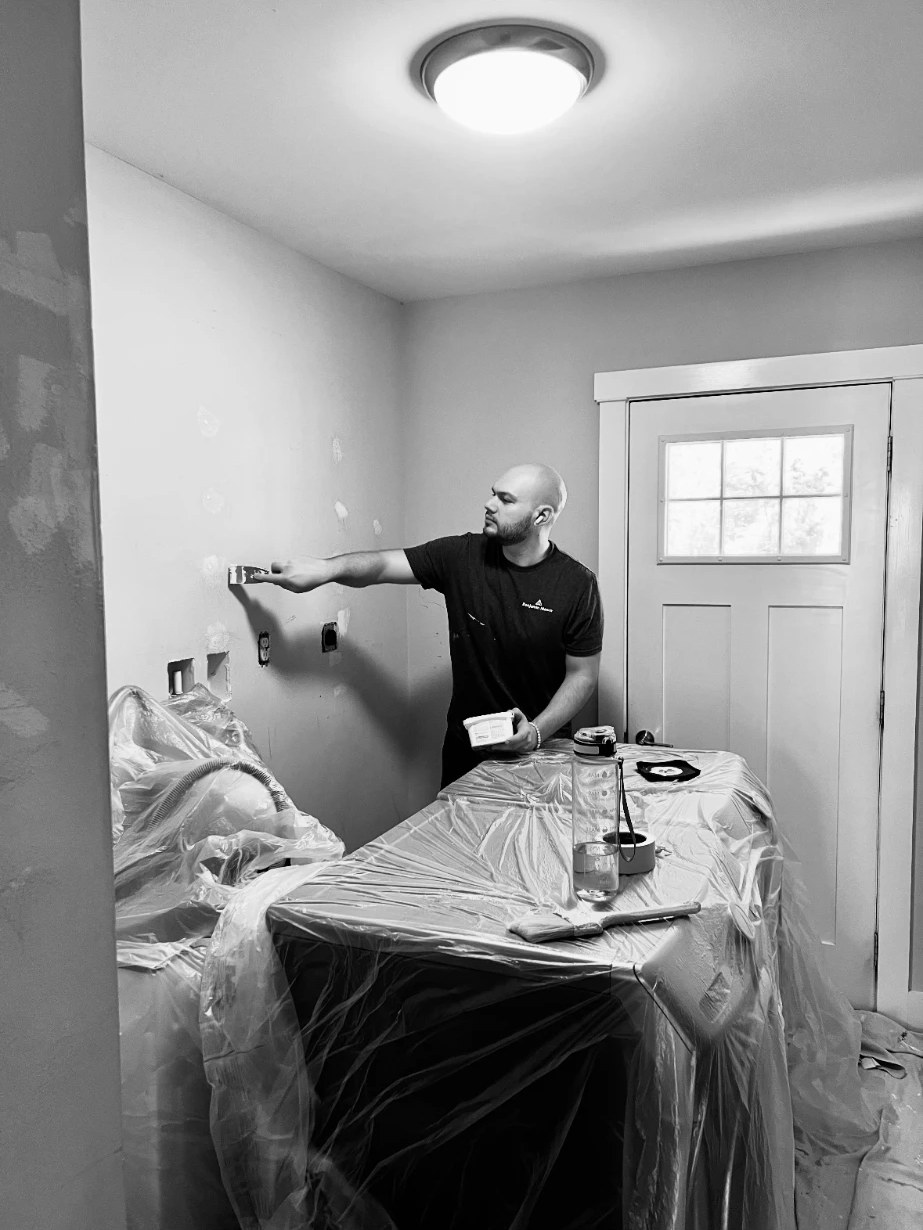Chris patching and prepping a wall in a room covered in protective plastic